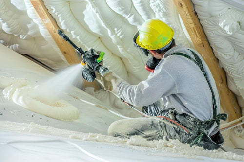 Construction worker applying polyurethane foam spray under roof decking
