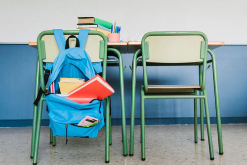 Student desks and chairs with a blue backpack and school supplies in a classroom