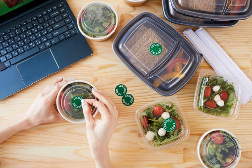 Assorted plastic food containers with prepared meals arranged on a worktable beside a laptop